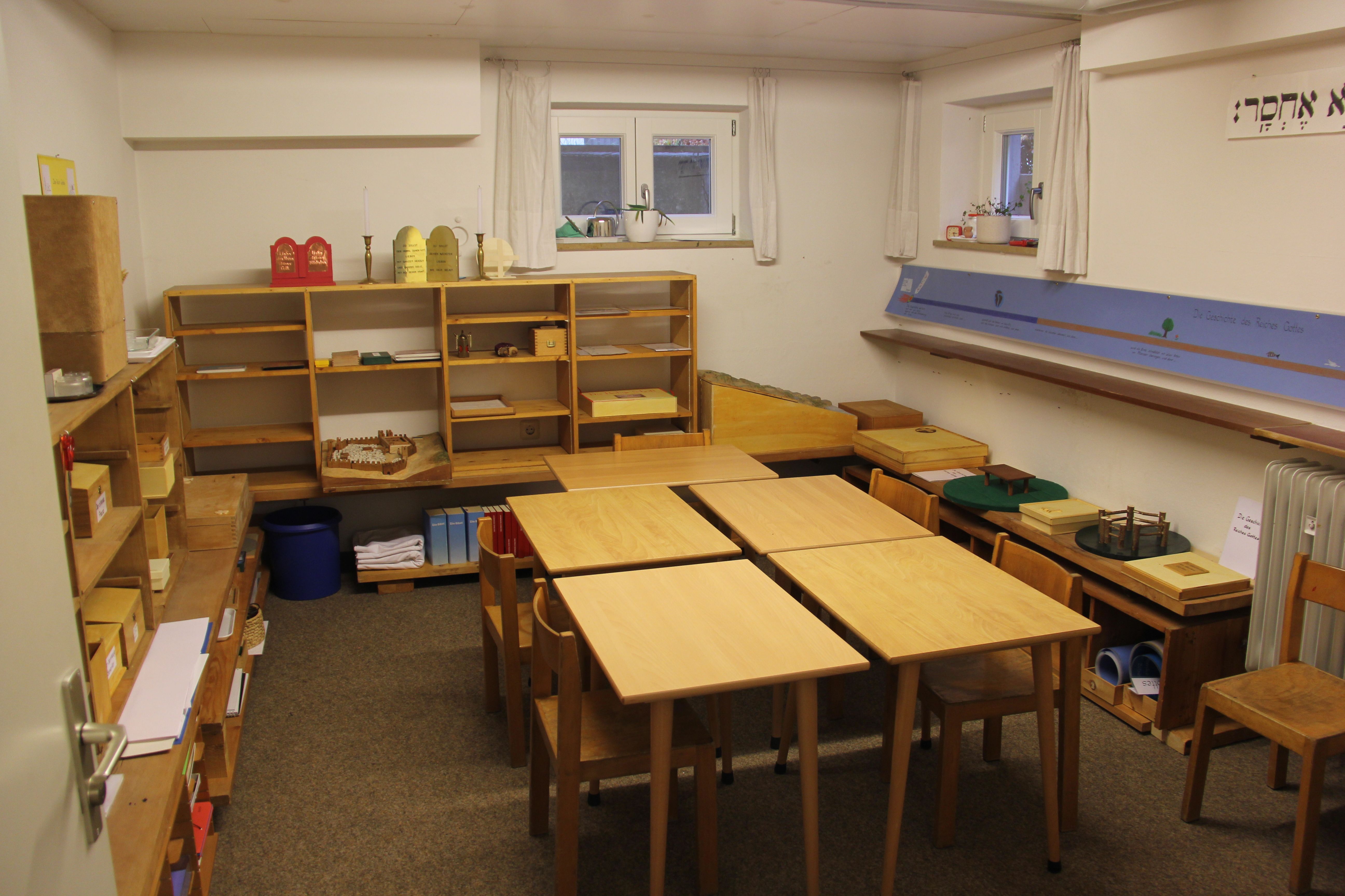 Das Atrium Stufe II ist ein Raum mit offenen Regalen mit katechetischem Material und mit dem Band von der Geschichte des Reiches Gottes an der Wand