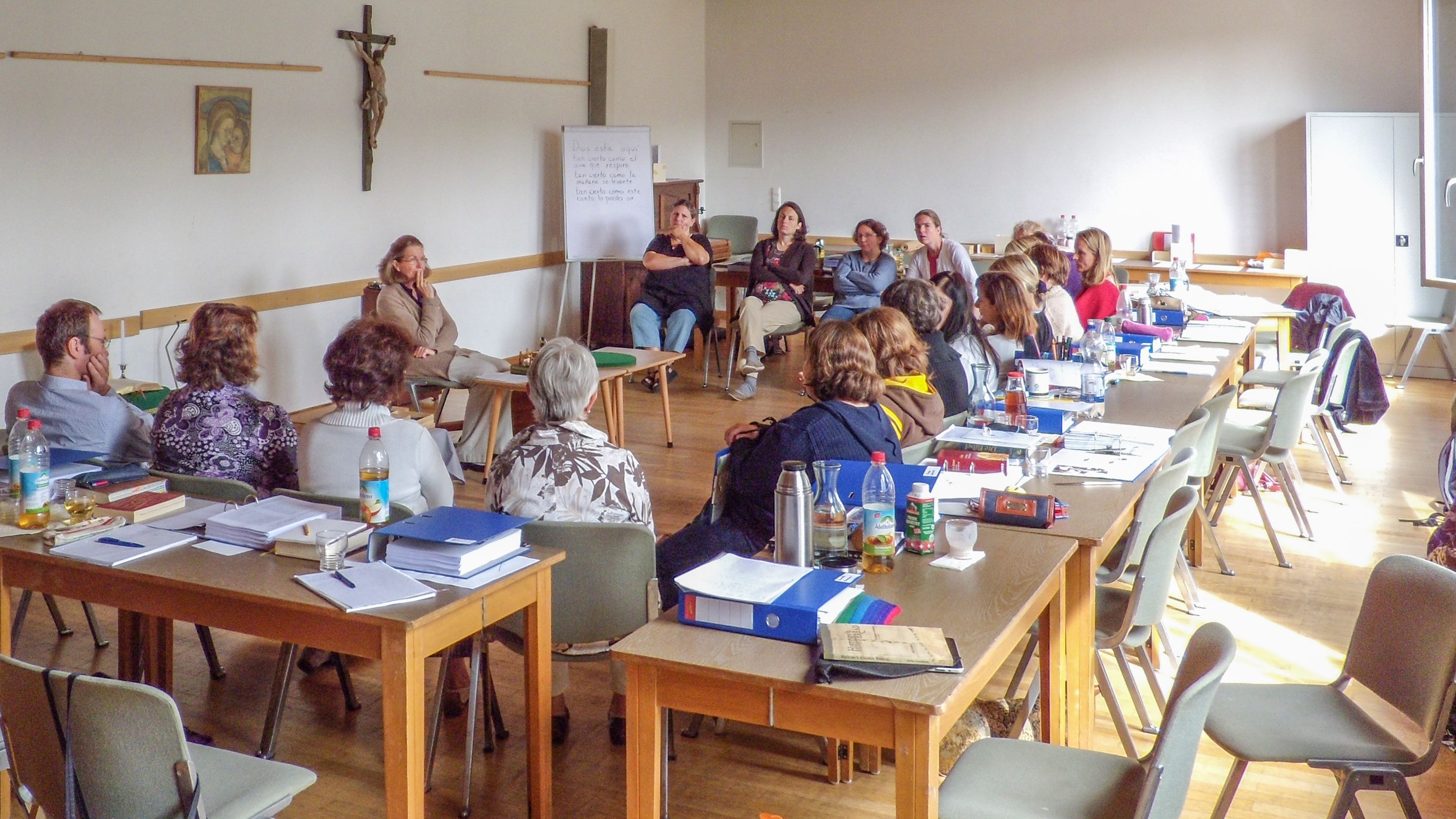 Pfarrsaal mit einem Tischkreis, innerhalb ein Stuhlkreis, die Kursteilnehmer hören bei der Präsentation eines Themas zu.