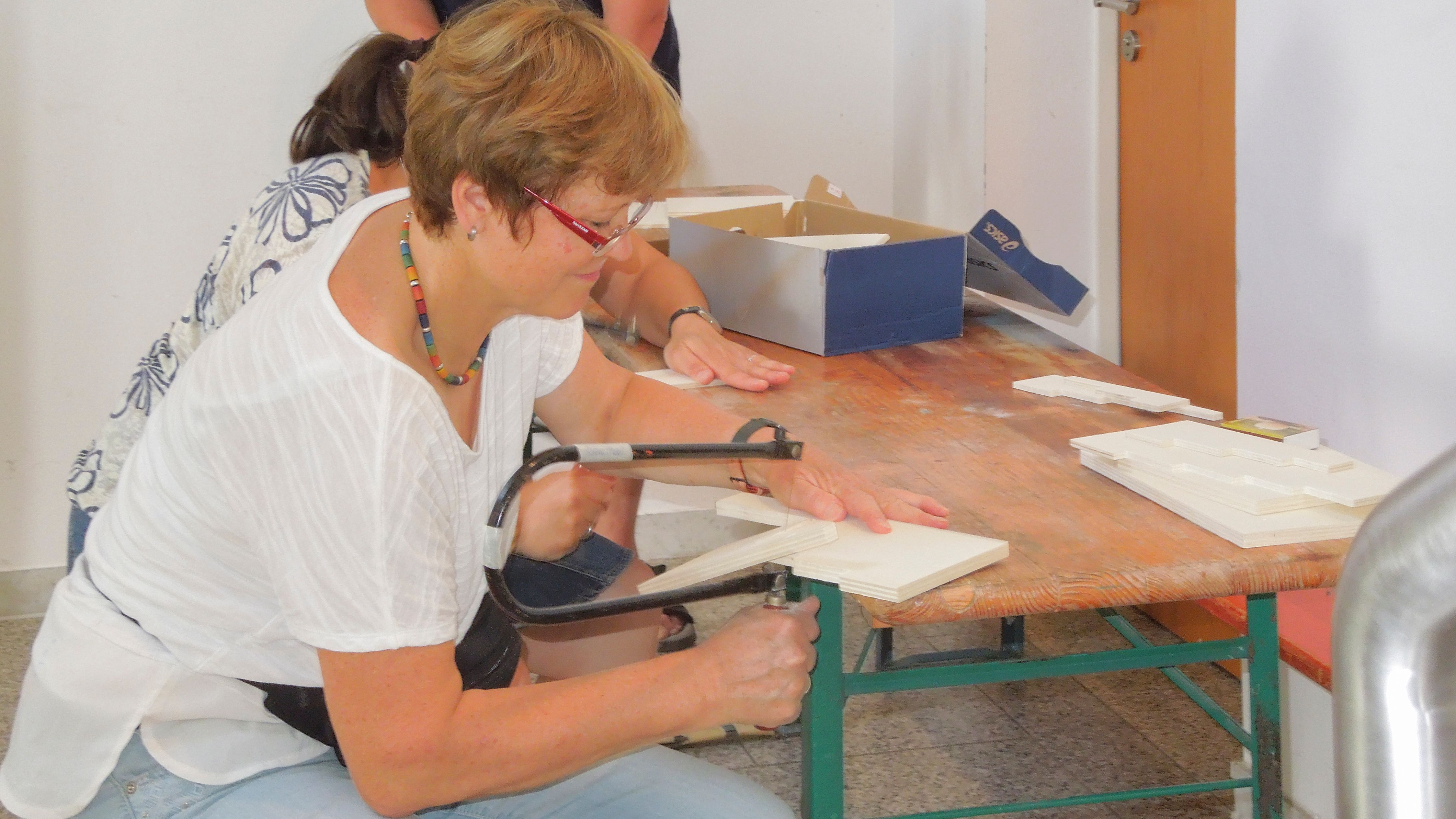 Eine Kursteilnehmerin sägt mit der Laubsäge Teile eines Materials aus Holz aus.