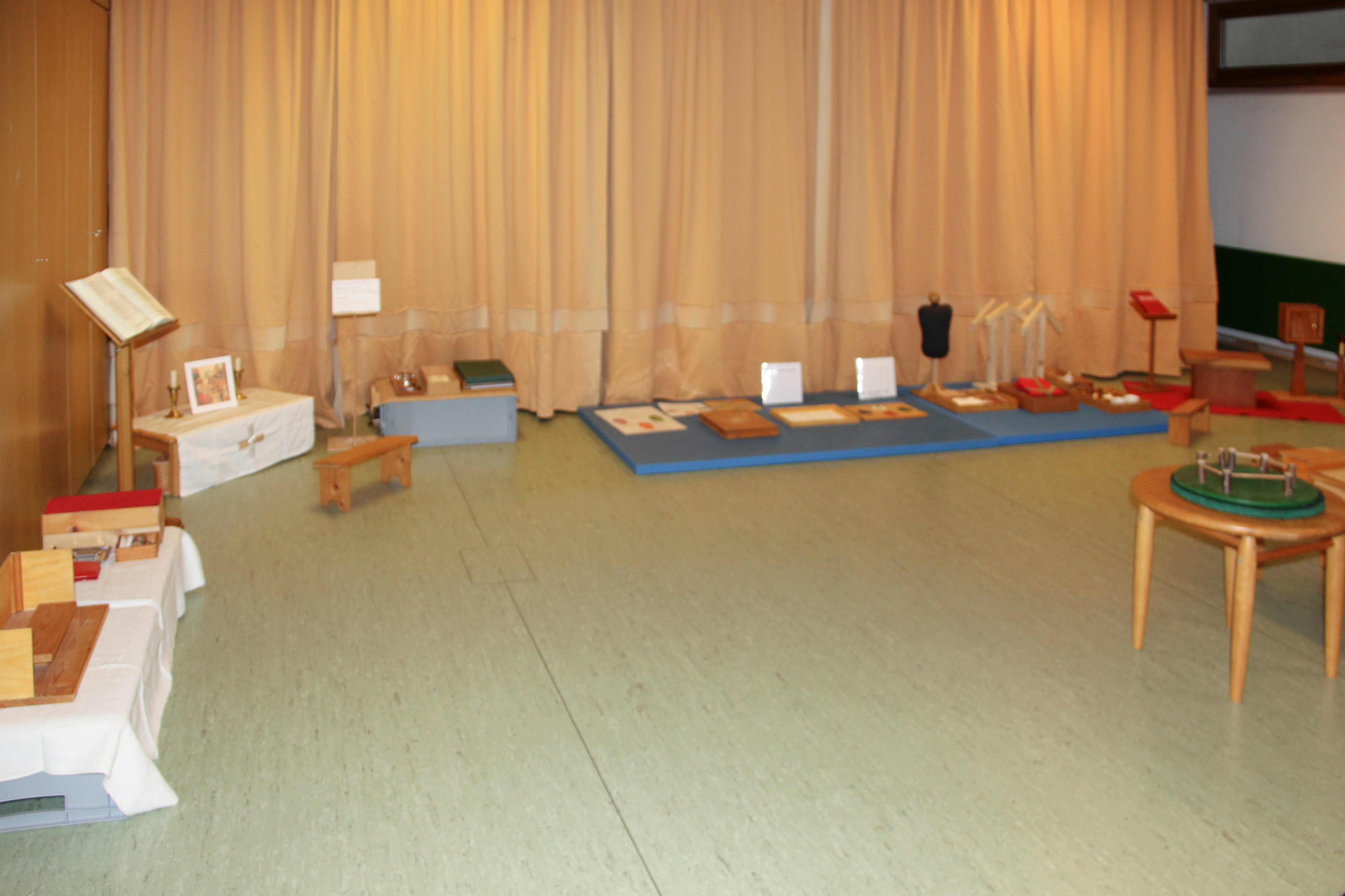 Ein Turnraum, in dem die Turngeräte mit einem Vorhang verdeckt und die Materialien auf kleinen Tischen und Matten ausgelegt sind, wird zum Atrium Stufe I.